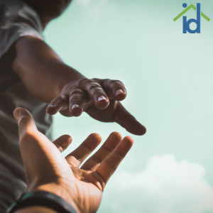 two hands reaching for each other with a blue sky in the background. A small house and id logo in the top right corner